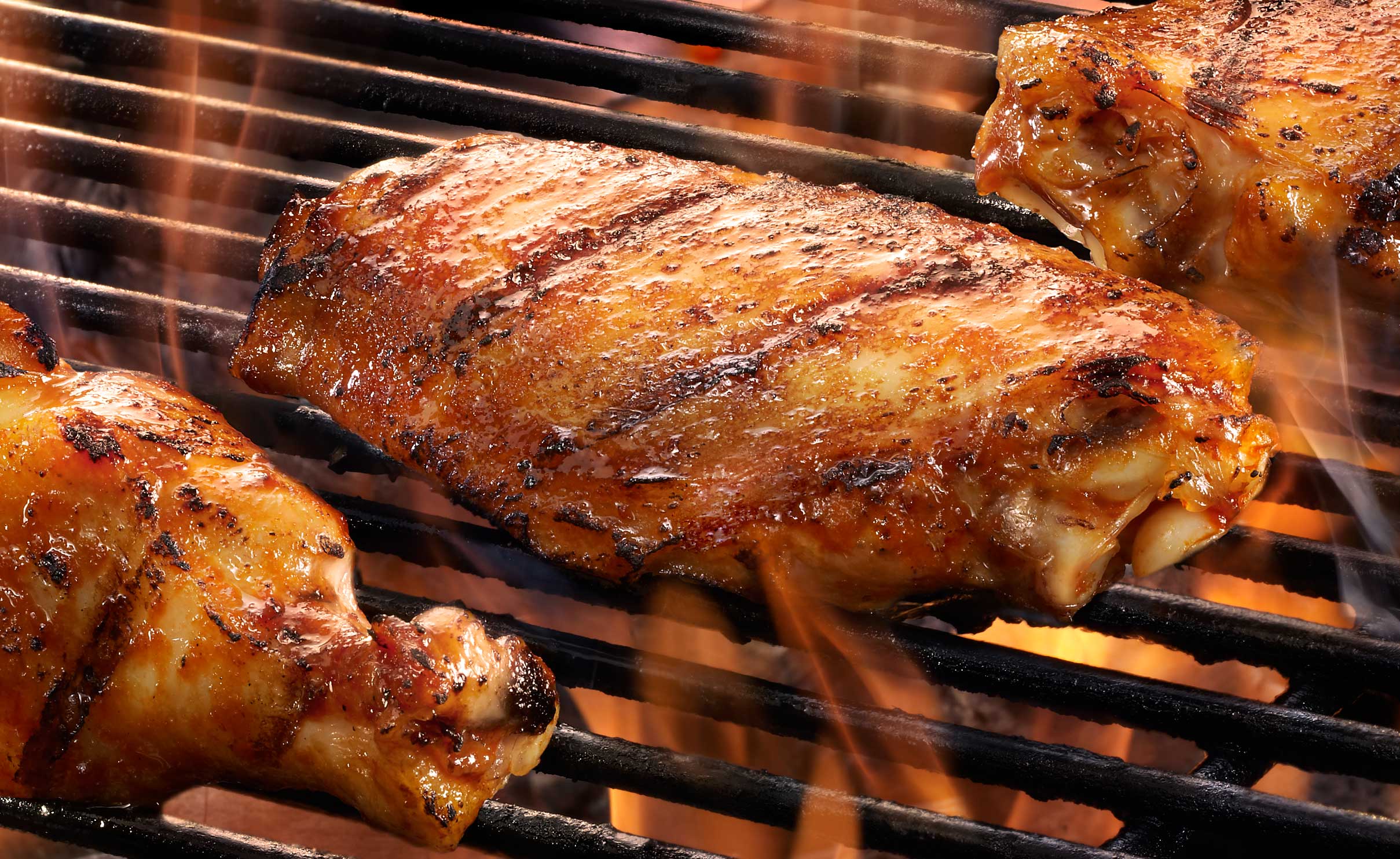 Three chicken breasts on flaming bar-B-Que grill